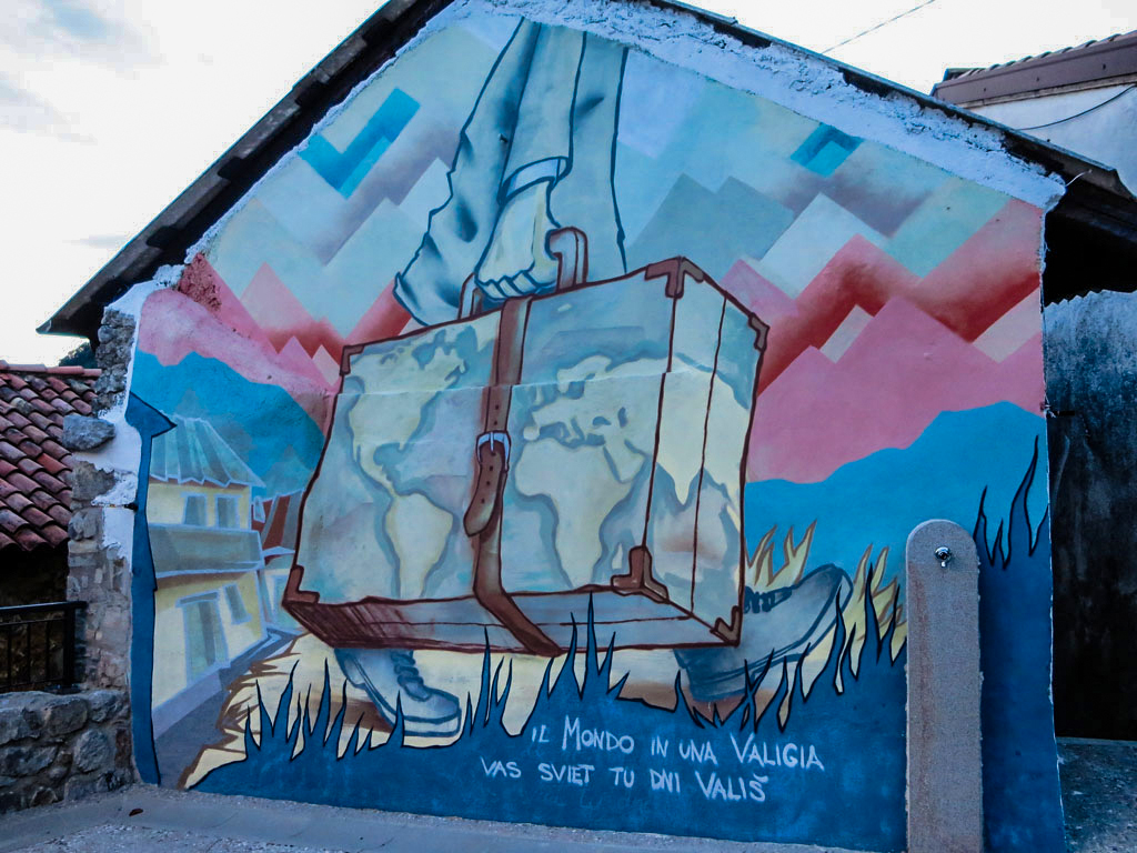 Murales in piazza a Drenchia che raffigura una persona con una valigia che parte